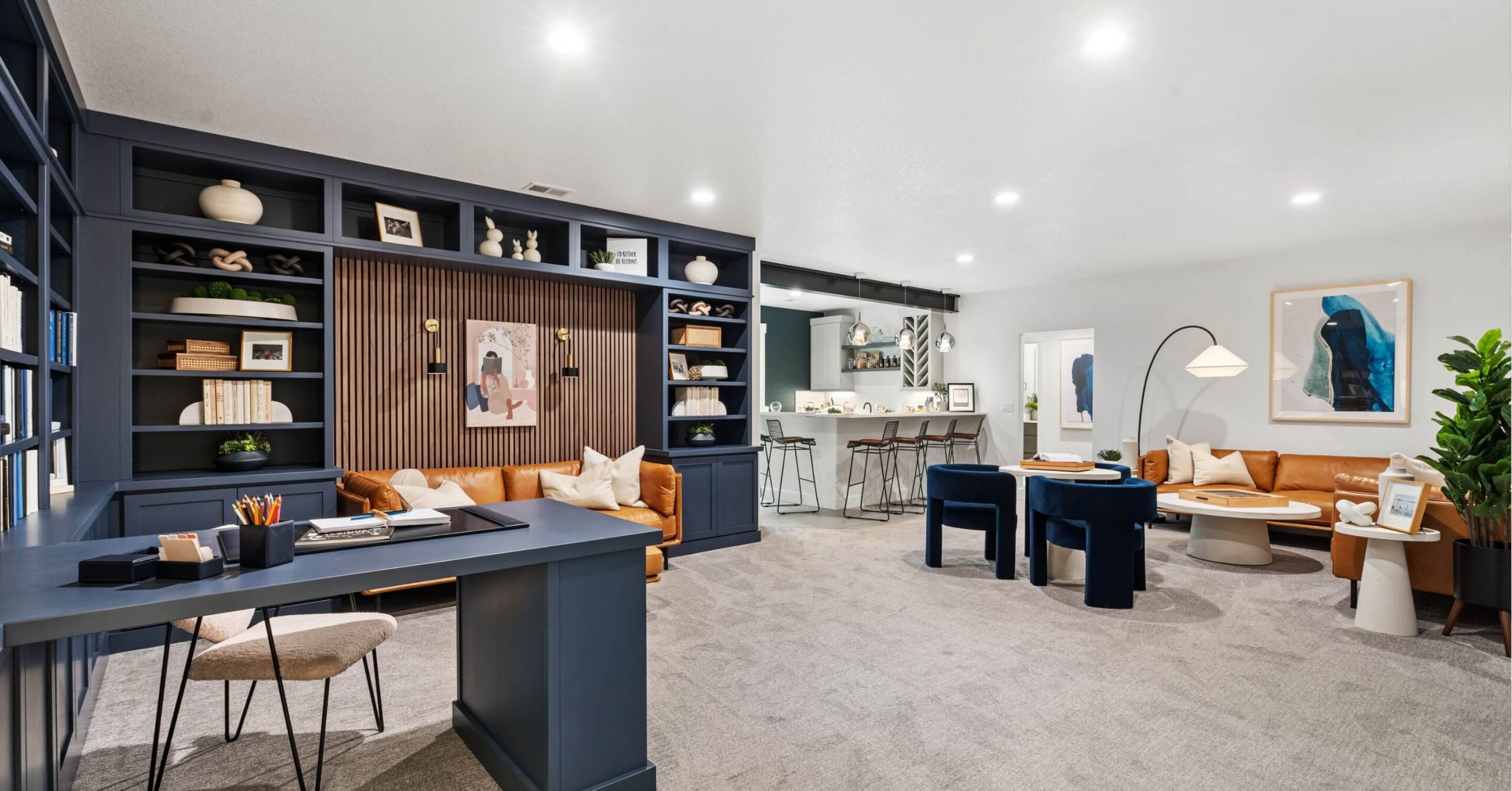 Modern living space with a navy bookshelf, leather sofa, and barstools at a counter reminiscent of those in Centerra restaurants. Round tables with chairs complement the neutral decor and framed art on walls. Bright lighting highlights the area’s sophistication.