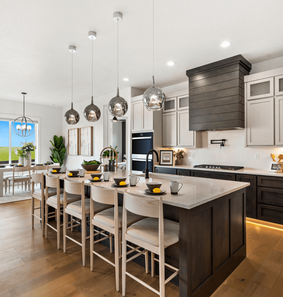 Modern kitchen with an island, bar stools, and pendant lights. Black and white cabinetry, stainless steel appliances, and wood flooring. Dining area visible in the background, reminiscent of the sleek designs found in Kinston Centerra's finest neighborhoods.