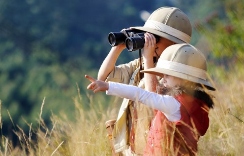 Two children in hats, certified wild, looking through binoculars.