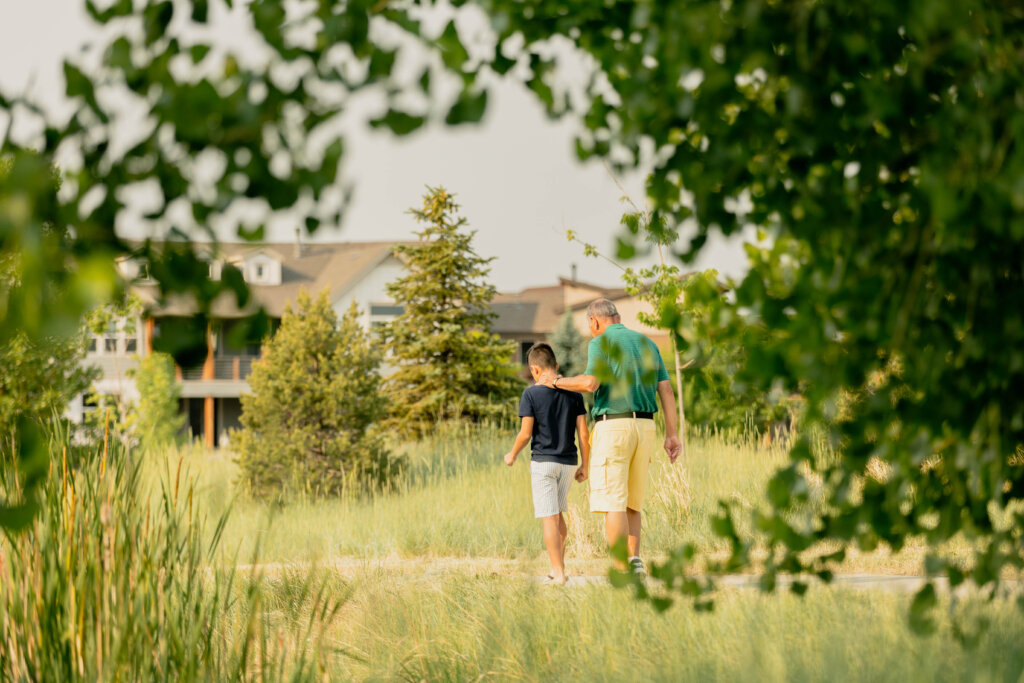 An adult and a child walk along a path surrounded by greenery, with new homes in Centerra, Loveland Colorado visible in the background.